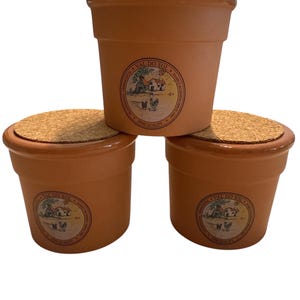 May include: Three terracotta flower pots with cork lids. Each pot has a circular label with the text "VAL DO SOL" and a graphic of a farm scene. The pots are a warm, earthy tone, suitable for planting.