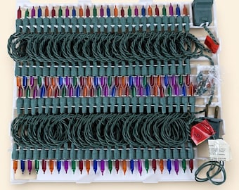 Puede incluir: Una cadena de luces navideñas en miniatura multicolores con cable verde oscuro, enrollada y organizada cuidadosamente en una bandeja de almacenamiento de plástico blanco. El juego incluye un enchufe estándar y una bolsa con bombillas de repuesto.