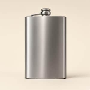 May include: A rectangular metal flask with a brushed silver finish and rounded edges. The flask features a screw-top cap attached to a hinged arm, which is secured to the top center of the container. The surface has a smooth, metallic texture.