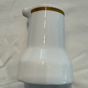 以下が含まれることがあります： 上部に金色のバンドが付いた白いセラミッククリーマー。クリーマーには小さな注ぎ口と丸みを帯びたベースがあります。 デザインはシンプルでクラシックで、クリームやミルクのサービングに適しています。