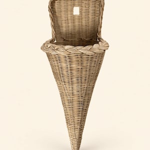 May include: A cone-shaped wall basket woven from light brown wicker. The basket features a flat back panel with a small square cutout for hanging and a thick, braided rim around the circular opening that tapers down to a pointed base.