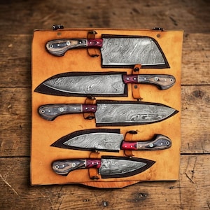 May include: A set of five Damascus steel knives with wooden handles and red accents, displayed in a tan leather case. The blades have a unique patterned design. The case has leather straps to secure the knives.