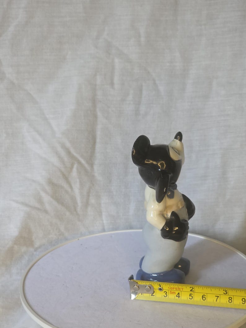 May include: A ceramic figurine of a black and white animal, possibly a cat or dog, holding a smaller black animal. The figurine has a light blue base and is approximately 3 inches tall.