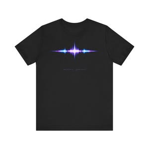 Può includere: T-shirt nero con grafica di un'onda sonora nei toni del blu e del viola. Il design include il testo "INDUSTRIAL FREQUENCY" sottostante. La maglietta è realizzata in un materiale morbido.