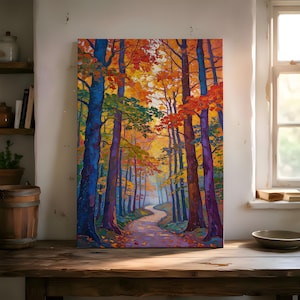 Puede incluir: Una pintura vibrante de una escena de bosque con un camino sinuoso. Los árboles muestran un espectro de colores, incluyendo azul, naranja, amarillo y verde, sugiriendo un paisaje otoñal. La obra de arte se exhibe sobre una mesa de madera.