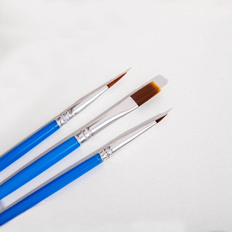 May include: Three paint brushes with bright blue wooden handles and silver metal ferrules. The brushes feature synthetic bristles in shades of brown and white, including one fine-tipped round brush, one flat brush, and one angled brush.