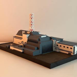 Könnte beinhalten: Detailliertes Architekturmodell eines Kraftwerks mit einem hohen, weiß-roten Gitterturm. Das Modell hat ein grau-beiges Farbschema mit schwarzem Sockel. Das Design umfasst mehrere Gebäude und Strukturen.