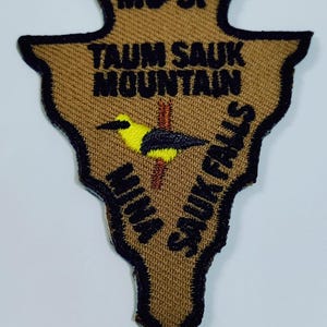May include: A brown and black embroidered patch with the text "MO-SP", "TAUM SAUK MOUNTAIN", "NINA SAUK FALLS". The patch features a yellow and black bird illustration. The patch has a black border.