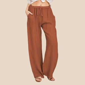 May include: Rust-colored wide-leg pants with a drawstring waist and pockets. The pants are made of a lightweight fabric, suitable for warm weather. The casual design offers comfort and style.