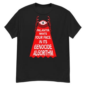 May include: A black short-sleeve t-shirt featuring a graphic of a stylized red eye emitting a beam of light. The text reads: PALANTIR WANTS YOUR FACE IN ITS GENOCIDE ALGORITHM. The design includes white lettering and red geometric accents.