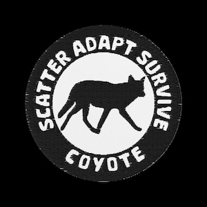 Peut inclure: Un écusson rond avec un bord noir et un centre blanc. Il présente une silhouette noire de coyote marchant vers la droite. Les mots "SCATTER ADAPT SURVIVE" sont en arc au-dessus, et "COYOTE" en dessous.