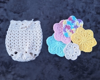 May include: A set of crocheted flower-shaped dishcloths in various colors, including pink, blue, yellow, and white. The dishcloths are arranged in a circle around a larger, white crocheted pouch.