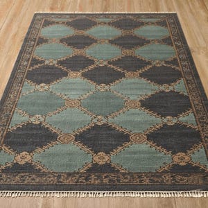 May include: A rectangular area rug featuring a repeating diamond pattern in dark charcoal and light teal. The design includes a tan floral lattice overlay connecting the shapes, a decorative border, and short white fringe along the short ends.