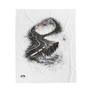 May include: White blanket featuring a black and white artistic rendering of a road winding along a cliff edge. The design includes a sky with hints of color and a logo in the lower left corner.