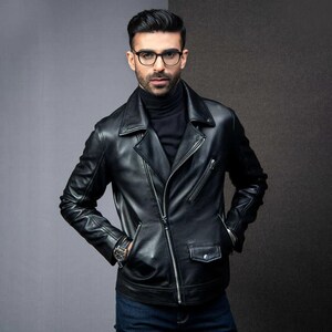 May include: A black leather jacket in a biker style, with a notched collar, an asymmetrical zip, and several pockets. The jacket is worn over a black roll neck. The model is wearing glasses and a watch.