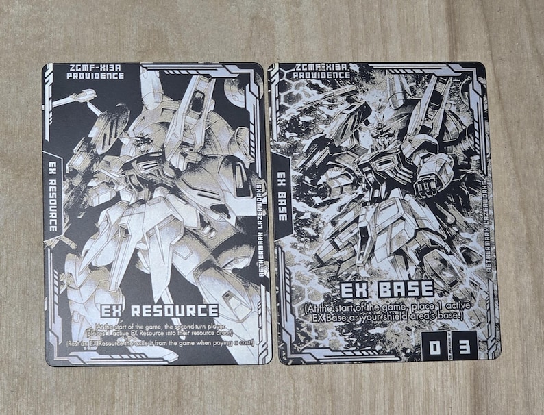 May include: Two trading cards featuring detailed black and white illustrations of a mecha. One card reads "EX RESOURCE" and the other "EX BASE". The cards have text and a number "03".