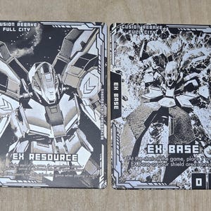 May include: Two trading cards with black and white illustrations of futuristic robots. The card on the left is labeled "EX RESOURCE" and the card on the right is labeled "EX BASE". The cards have text that reads "CUSION REBAKE FULL CITY".