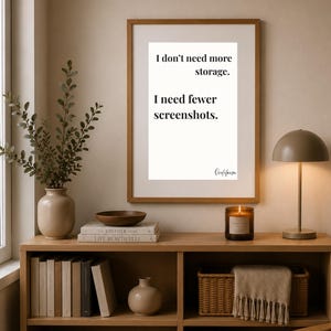 Puede incluir: Una lámina de arte enmarcada con fondo blanco y texto negro que dice: I don't need more storage. I need fewer screenshots. La lámina se muestra en un marco de madera marrón fino colgado en una pared sobre una estantería de madera.