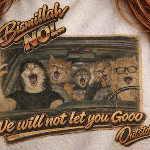 Peut inclure: T-shirt blanc avec un motif humoristique de chats dans une voiture, hurlant. Le texte dit "Bismillah NO!" et "We will not let you Gooo Outside". Le graphisme a un aspect vintage et vieilli.