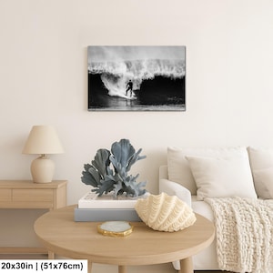 K&ouml;nnte beinhalten: Schwarz-Wei&szlig;-Leinwanddruck eines Surfers, der eine gro&szlig;e Welle reitet. Das Kunstwerk ist 51x76cm gro&szlig;. Der Surfer ist eine Silhouette vor der Welle. Der Druck wird &uuml;ber einem runden Holztisch mit dekorativen Gegenst&auml;nden angezeigt.