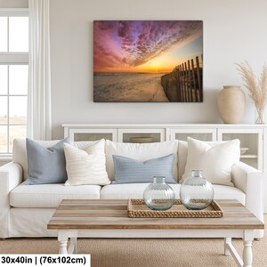 Peut inclure: Impression sur toile d'une sc&egrave;ne de plage au coucher du soleil. Le ciel est un m&eacute;lange de roses, d'oranges et de violets. Une cl&ocirc;ture en bois borde la plage. L'impression mesure 76x102cm.