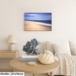 May include: A framed canvas print of a beach scene with a blurred effect. The image features a sandy beach, ocean waves, and a blue sky. The print measures 20x30 inches (51x76cm).