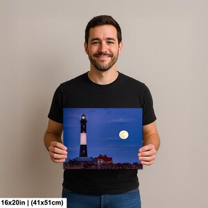 May include: A framed print of a lighthouse at dusk. The black and white lighthouse stands tall against a deep blue sky, with a full moon visible. The print measures 16x20 inches.