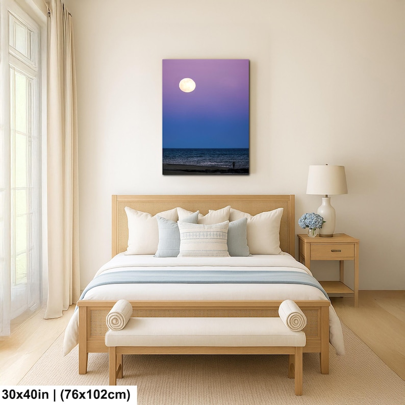 May include: A canvas print depicting a nighttime beach scene with a large, bright moon in a purple and blue sky. The artwork is displayed above a bed with light-colored bedding and a wooden frame. The print measures 30x40 inches.