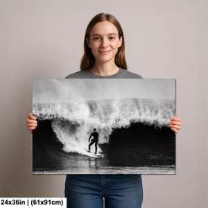 K&ouml;nnte beinhalten: Schwarz-Wei&szlig;-Leinwanddruck eines Surfers auf einer Welle. Das Kunstwerk misst 61x91cm (24x36 Zoll). Der Surfer, in einem schwarzen Neoprenanzug, reitet auf einem wei&szlig;en Surfbrett. Die Welle bricht und erzeugt eine dramatische Szene.