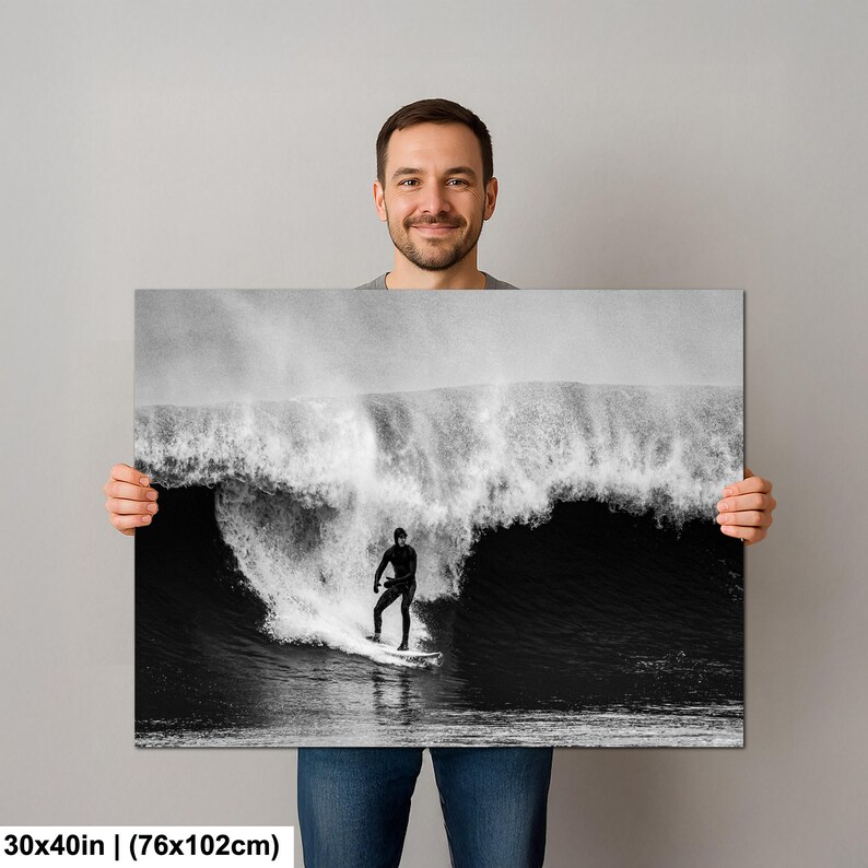 K&ouml;nnte beinhalten: Schwarz-Wei&szlig;-Fotografie eines Surfers, der eine gro&szlig;e Welle reitet. Der Surfer tr&auml;gt einen schwarzen Neoprenanzug und steht auf einem Surfbrett. Die Welle bricht und erzeugt eine Wasserwand. Die Leinwand misst 76x102cm.