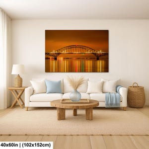 May include: A large canvas print of a bridge at night, with lights reflecting in the water. The print is 40x60 inches (102x152cm) and hangs above a white sofa in a living room setting. The color palette is warm, with orange and gold tones.