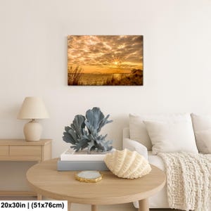 May include: A 20x30 inch (51x76cm) canvas print of a sunset over water. The sky is filled with golden clouds, and the sun's rays burst through. The print is displayed above a round wooden table with decorative items.