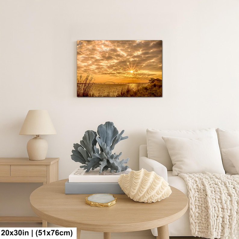 May include: A 20x30 inch (51x76cm) canvas print of a sunset over water. The sky is filled with golden clouds, and the sun's rays burst through. The print is displayed above a round wooden table with decorative items.