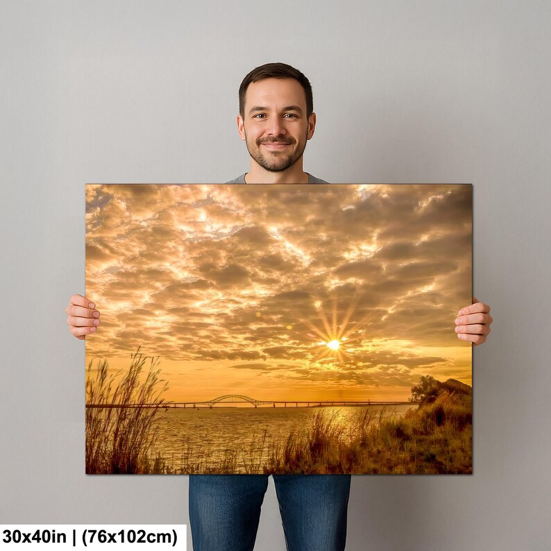 May include: A canvas print featuring a vibrant sunset over a body of water, with a bridge in the distance. The sky is filled with golden clouds, and the sun is shining brightly. The print measures 30x40 inches.