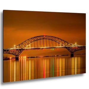 May include: A nighttime photograph of a bridge with a curved arch design. The bridge is illuminated with lights, reflecting in the water below. The sky is a warm orange color, and the overall scene is a vibrant display of light and color.