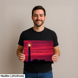 Może przedstawiać: Wydruk na pł&oacute;tnie 16x20 cali (41x51cm) przedstawiający latarnię morską o zachodzie słońca. Latarnia jest wysoka i smukła, z jasnym światłem na szczycie. Niebo jest żywo czerwone i r&oacute;żowe, z sylwetkami budynk&oacute;w.