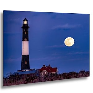May include: A nighttime landscape featuring a tall lighthouse with a black and white tower, a red-roofed building, and a full moon in a dark blue sky. The lighthouse is illuminated, and the scene evokes a sense of tranquility and maritime history.