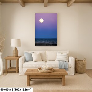 May include: A vertical canvas print depicts a serene beach scene at dusk. The sky transitions from purple to blue, with a full moon. The ocean meets the shore, and a silhouetted figure stands on the beach. The canvas measures 40x60 inches.