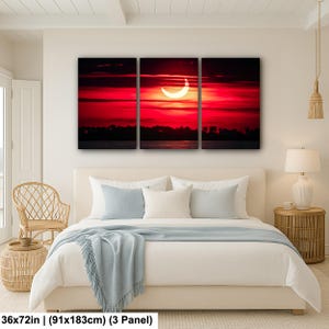 Pode incluir: Uma impress&atilde;o em tela de tr&ecirc;s pain&eacute;is que retrata um vibrante p&ocirc;r do sol vermelho com um sol em forma de crescente. A obra apresenta uma silhueta escura de &aacute;rvores e &aacute;gua na parte inferior. Dimens&otilde;es: 91x183cm.