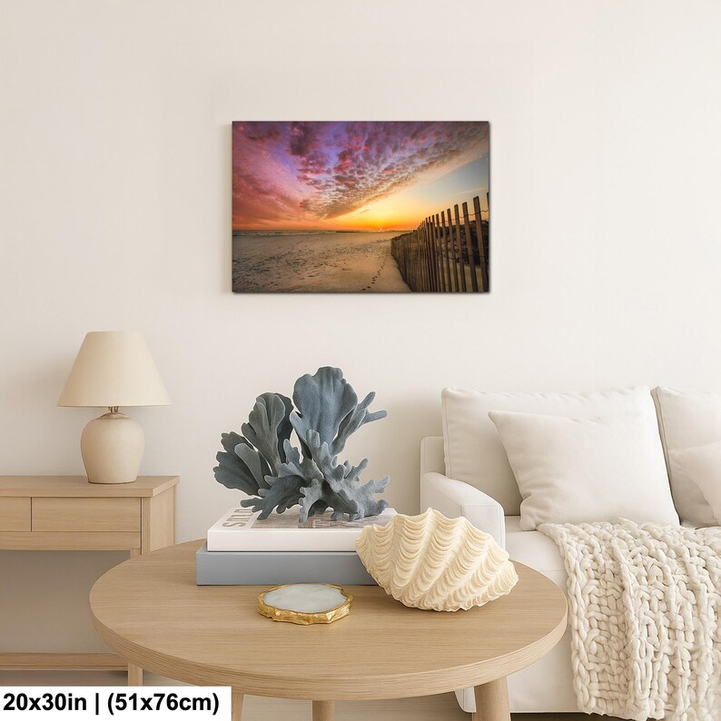 Peut inclure: Impression sur toile d'une sc&egrave;ne de plage au coucher du soleil. Le ciel est rempli de couleurs vives de rose, de violet et d'orange. Une cl&ocirc;ture en bois longe le c&ocirc;t&eacute; droit de la plage. Dimensions : 51x76cm.