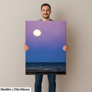 May include: A canvas print featuring a vibrant night scene. The artwork depicts a full moon in a gradient sky above a dark ocean and a silhouetted figure on the beach. The canvas measures 30x40 inches.