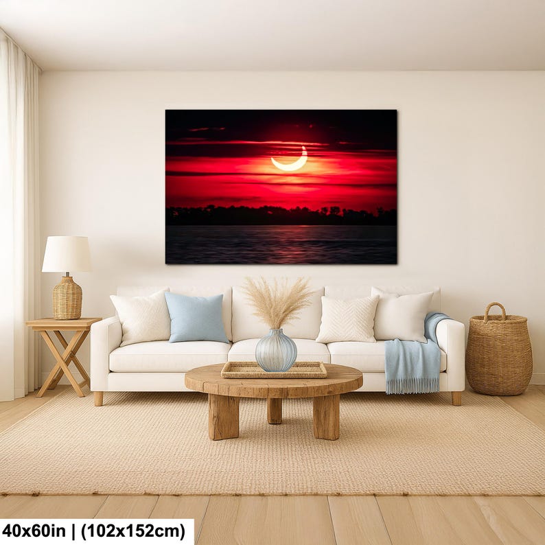 Pode incluir: Uma grande impress&atilde;o em tela retrata um vibrante p&ocirc;r do sol vermelho com uma forma de lua crescente. A obra de arte, medindo 102x152cm, est&aacute; pendurada acima de um sof&aacute; branco em uma sala de estar. A cena inclui um corpo de &aacute;gua e um horizonte escuro.