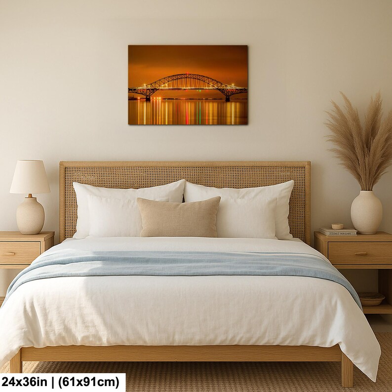 May include: A framed canvas print of a bridge at night, with lights reflecting in the water. The artwork is 24x36 inches. The bridge has an arched design and is illuminated with warm-toned lights against a dark sky.
