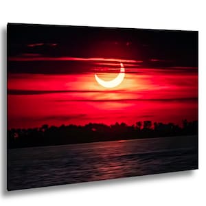 Pode incluir: Uma imagem vibrante de um eclipse solar, mostrando uma crescente brilhante contra um c&eacute;u vermelho ardente. A cena inclui uma silhueta escura de &aacute;rvores e &aacute;gua, criando um contraste dram&aacute;tico.