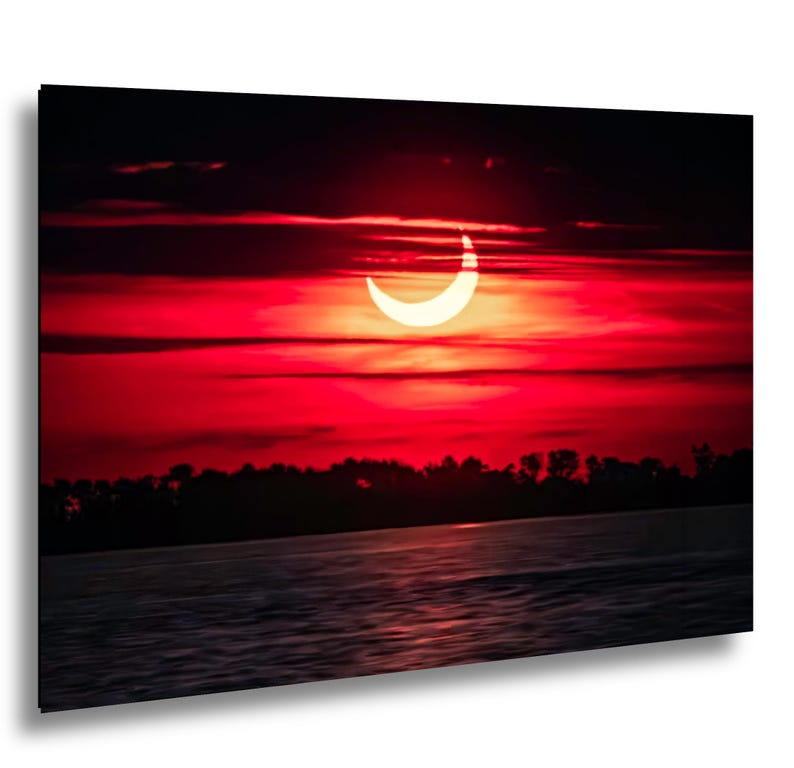 Pode incluir: Uma imagem vibrante de um eclipse solar, mostrando uma crescente brilhante contra um c&eacute;u vermelho ardente. A cena inclui uma silhueta escura de &aacute;rvores e &aacute;gua, criando um contraste dram&aacute;tico.