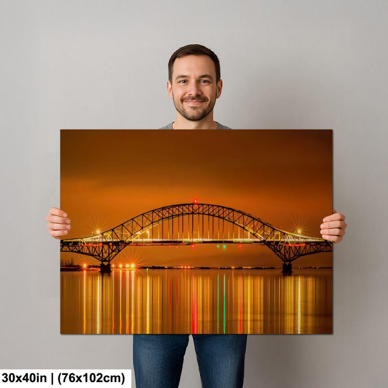 May include: A canvas print of a bridge at night, with the dimensions 30x40 inches. The bridge is illuminated with lights, reflecting in the water below. The sky is a warm orange color.