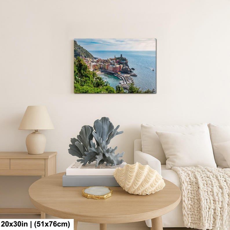 May include: A framed canvas print of a coastal Italian village, measuring 20x30 inches. The artwork depicts colorful buildings nestled along the shoreline, with a harbor and a tower. The scene is set under a blue sky with a few clouds.