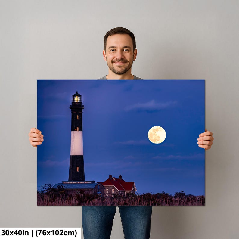 May include: A canvas print featuring a lighthouse under a full moon. The lighthouse is black and white with a red-roofed building at its base. The moon is a bright yellow orb against a deep blue sky. The print measures 30x40 inches.