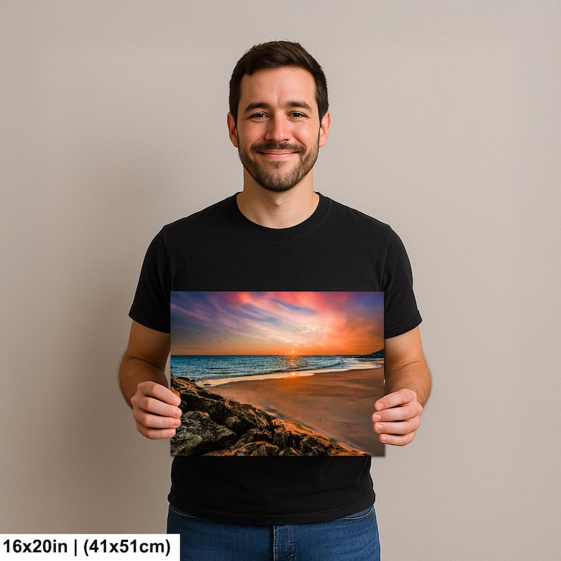 May include: A 16x20 inch (41x51cm) print of a beach scene at sunset. The image features a vibrant sky with shades of pink, orange, and blue, reflecting on the ocean. The foreground shows a rocky shoreline and sandy beach.