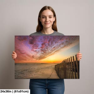 Peut inclure: Impression sur toile d'une sc&egrave;ne de plage au coucher du soleil. Le ciel est rempli de couleurs vives d'orange, de rose et de violet. Une cl&ocirc;ture en bois longe le c&ocirc;t&eacute; droit de la plage. L'impression mesure 61x91cm.